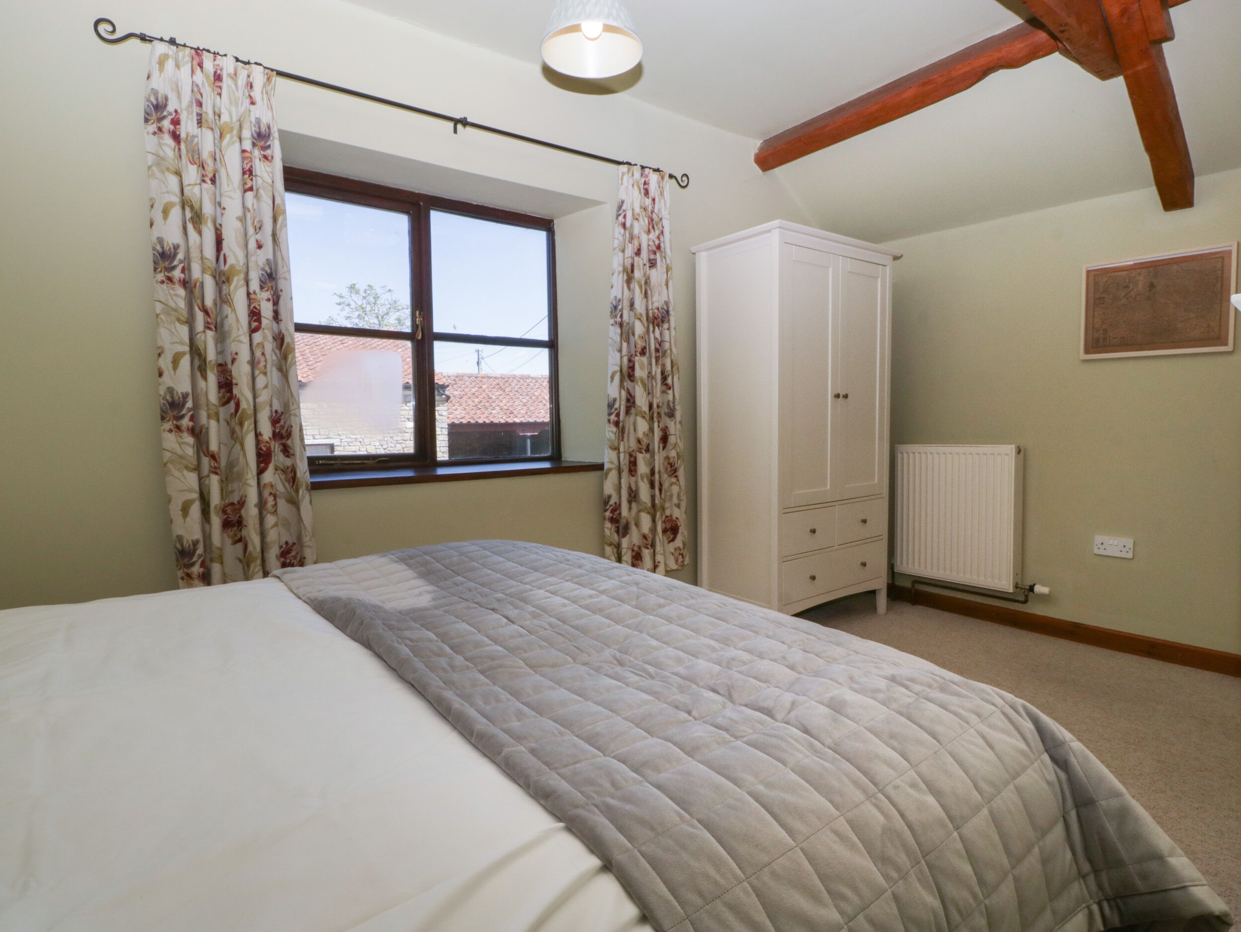 A bedroom with a bed, a window with curtains, a wardrobe, and a radiator.