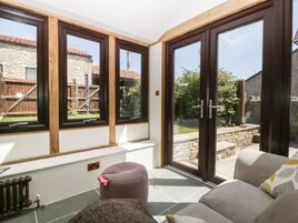 Una habitación soleada con un sofá, un pequeño reposapiés y un radiador.