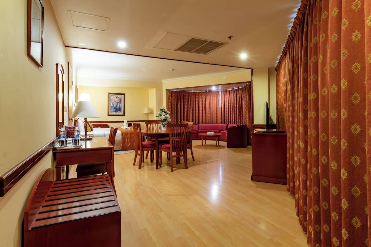 A hotel room with a wooden dining table, chairs, a sofa, and a TV.