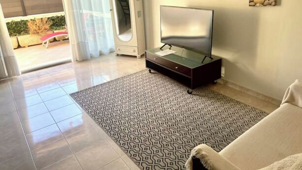 A modern living room with a flat-screen TV on a stand, a patterned rug, and a sofa. - Deux Pièces Avec Terrasse et Parking au Calme (Cagnes-sur-Mer)