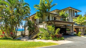 Une maison à deux étages avec un porche couvert, un escalier et un véhicule garé dans l’allée.
