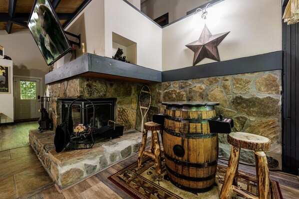Un interior rústico con chimenea de piedra, taburetes de barril de madera y una decoración de estrella en la pared.