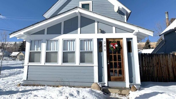 Ein zweigeschossiges Haus mit einer Veranda, einer Holztür und einem Wreath, sowie der Hausnummer 201.