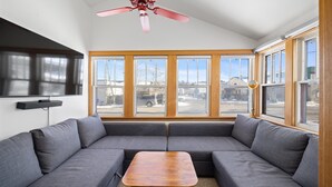 Ein modernes Wohnzimmer mit einem grauen Ecksofa, einem Holztisch und großen Fenstern mit Blick ins Freie.