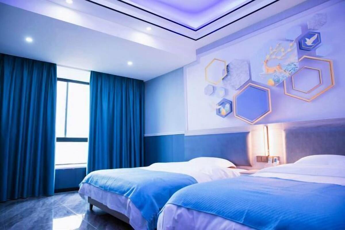A hotel room with two beds, a large window with curtains, and a wall with hexagonal decorations.