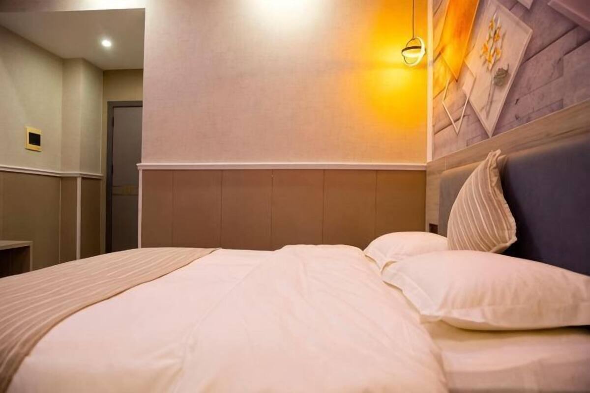 A hotel room with a bed, a headboard, a wall-mounted light, and a door.