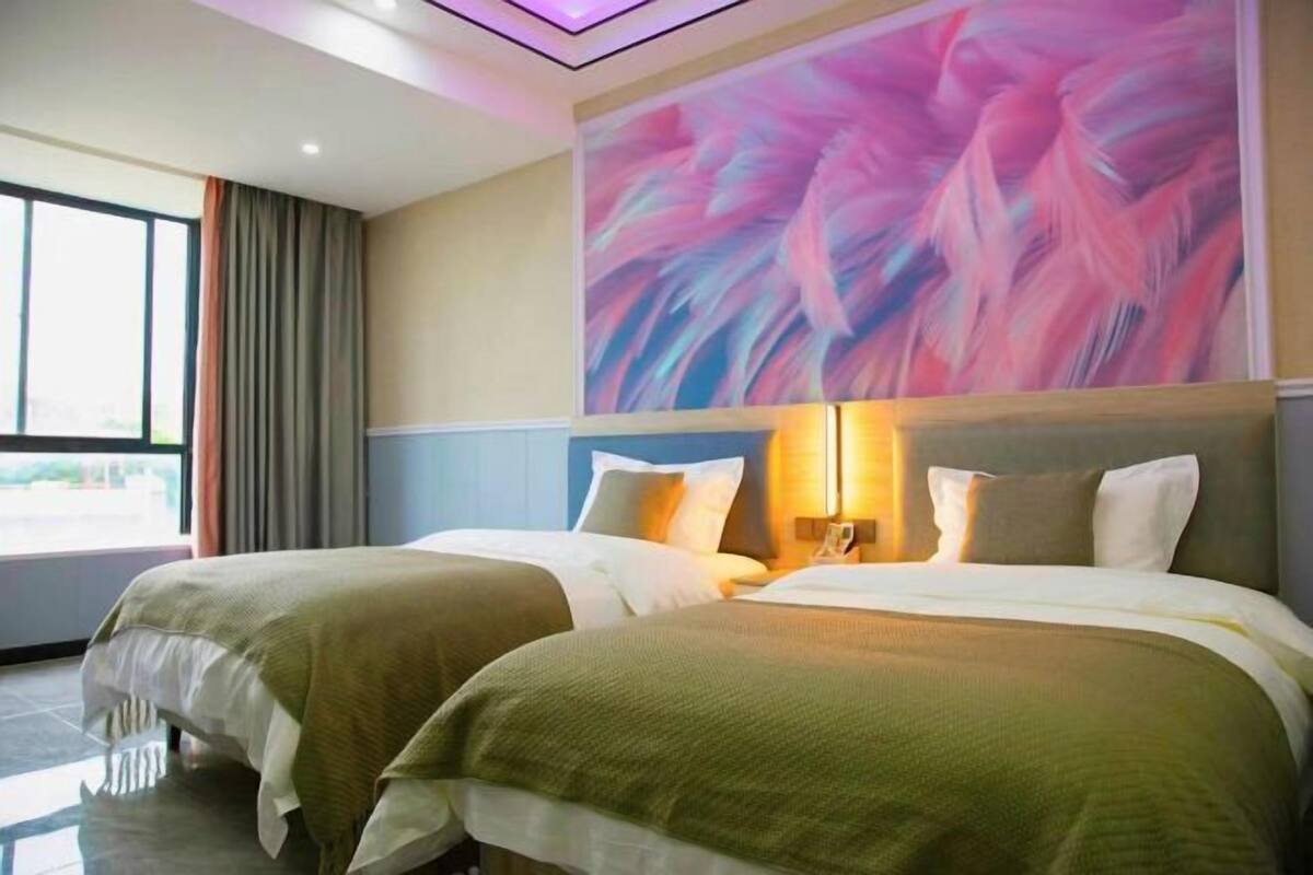 A hotel room with two beds, a large abstract painting on the wall, and a view of the outdoors through the window.