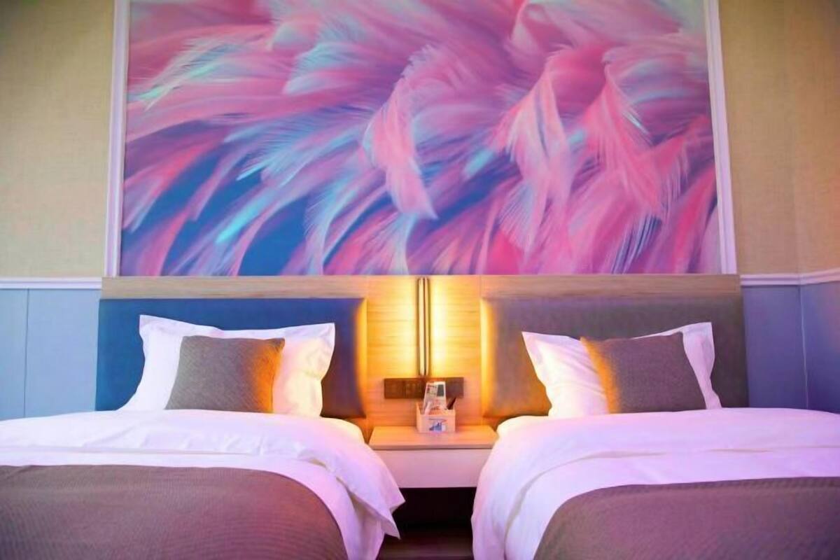 A hotel room with two beds, a nightstand, a wall-mounted lamp, and a large abstract painting.