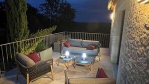 An outdoor patio area with a sofa, two chairs, and two small tables, all illuminated by wall-mounted lights. - Typical house with dovecote, swimming pool, summer kitchen, close to vineyards (Courrech, GREZELS)