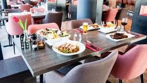A restaurant with multiple tables, each set with plates of food, glasses, and cutlery. - Bastion Hotel Amersfoort (Amersfoort)