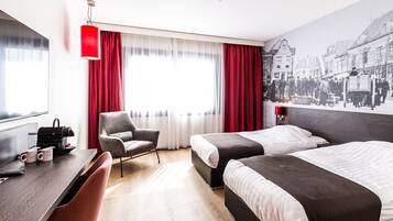 A hotel room with two beds, a desk, a chair, and a large window with red curtains.