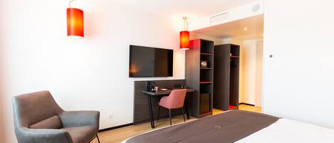 Quarto de hotel moderno com cama, escrivaninha, cadeira e televisão.