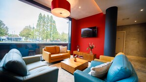A modern living room with a red accent wall, a flat-screen TV, and a large window overlooking a parking area. - Bastion Hotel Amersfoort (Amersfoort)