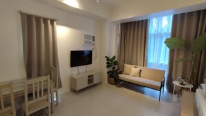 Een moderne woonkamer met een flatscreen televisie, een bank, een eettafel en een potplant.