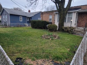 A residential lawn with a small garden bed, a tree, and a chain-link fence.