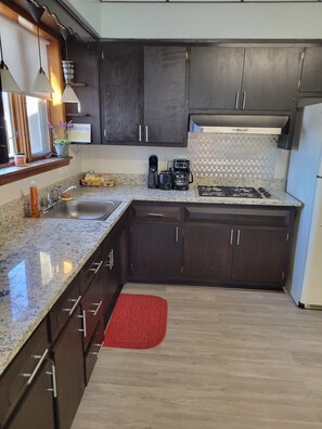 A kitchen with dark wooden cabinets, a granite countertop, a gas stove, a coffee maker, and a red rug.