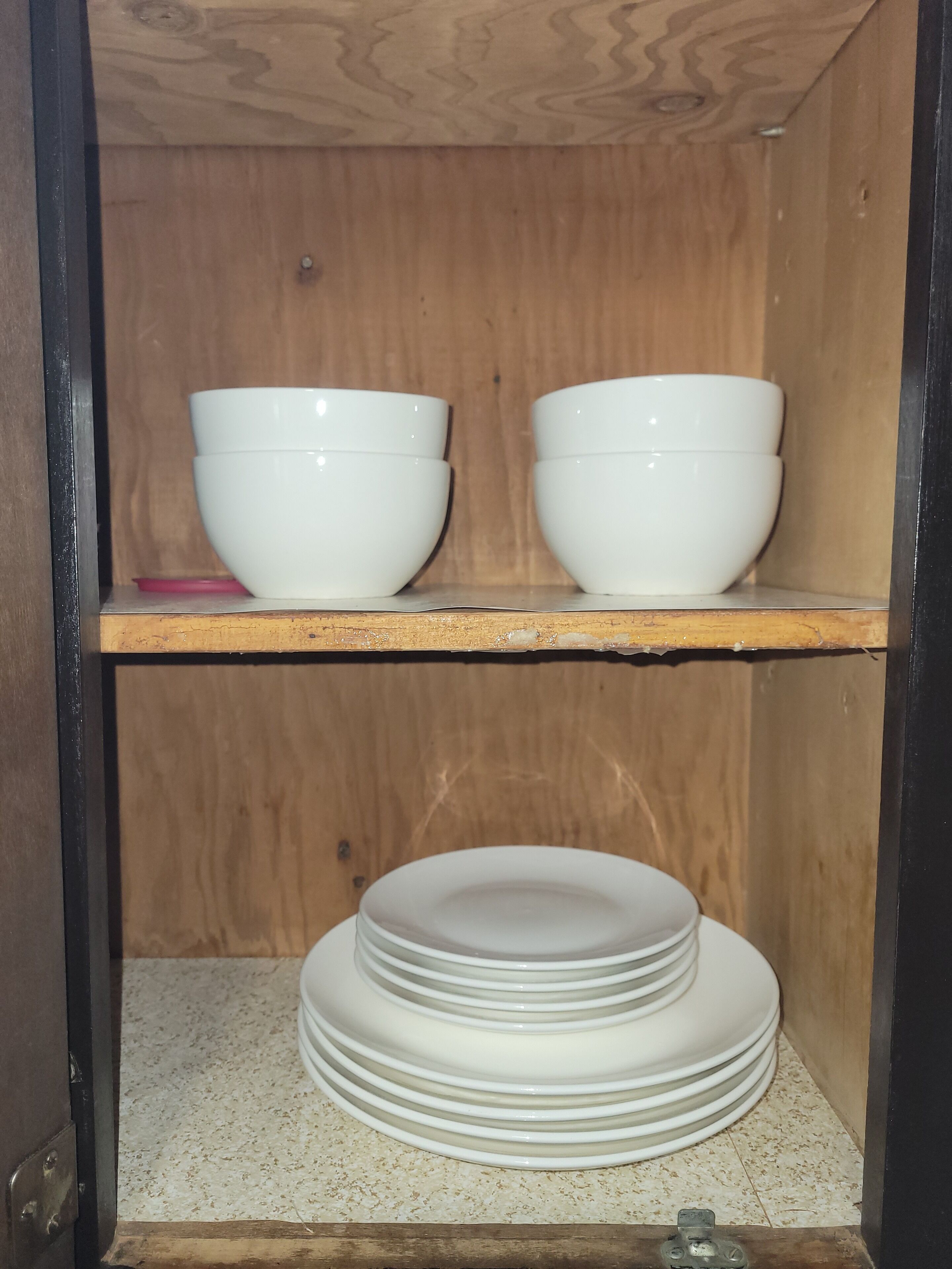 Ein Holzschrank mit zwei weißen Schüsseln auf der obersten Ablage und einem Stapel weißer Teller auf der untersten Ablage.