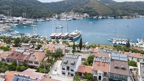 A marina with multiple boats docked, surrounded by residential buildings with red-tiled roofs and solar panels. - DUYGU APART (Fethiye)