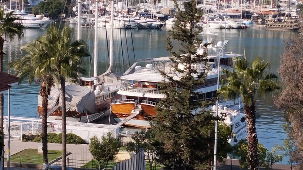 A marina with multiple boats docked, surrounded by palm trees and buildings in the background. - DUYGU APART (Fethiye)