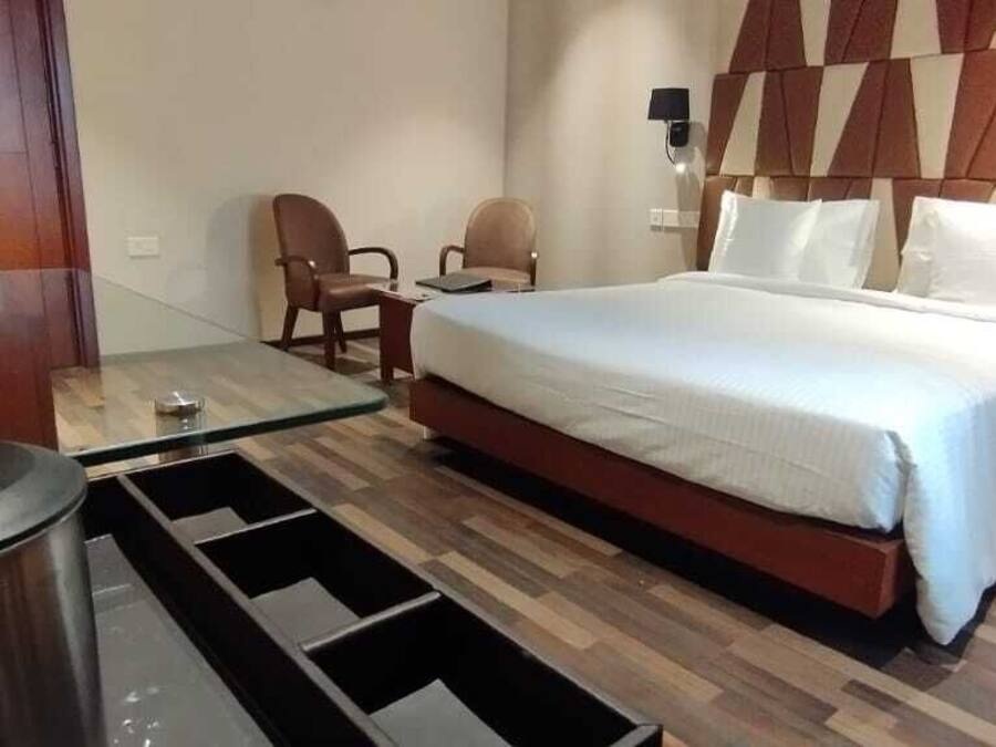 A hotel room with a bed, two chairs, a small table, a trash bin, and a nightstand with a phone.