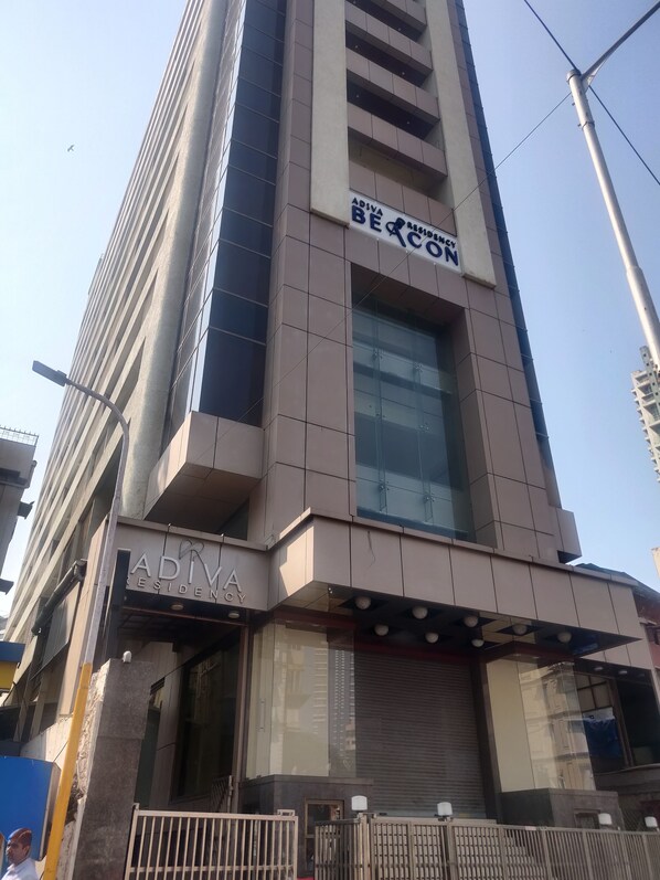 A modern building with a prominent 'ADIVA RESIDENCY' sign, large windows, and a gated entrance.