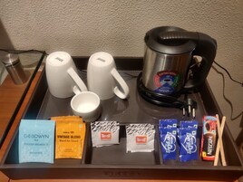Una bandeja con una cafetera, dos tazas blancas, una taza blanca más pequeña y diferentes paquetes de té y café.
