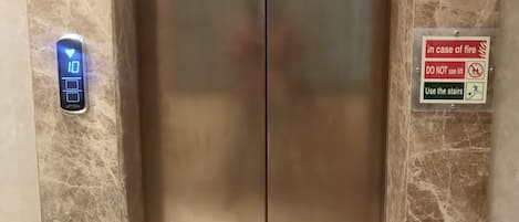 An elevator with a digital display showing '10' and a sign instructing to use stairs in case of fire.
