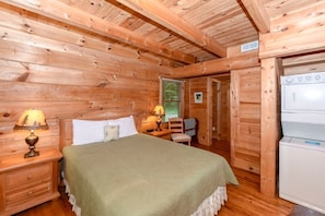 A wooden cabin room with a bed, nightstands, a chair, and a refrigerator. - Creekside 2 Bedroom Cabin by RedAwning (Townsend)