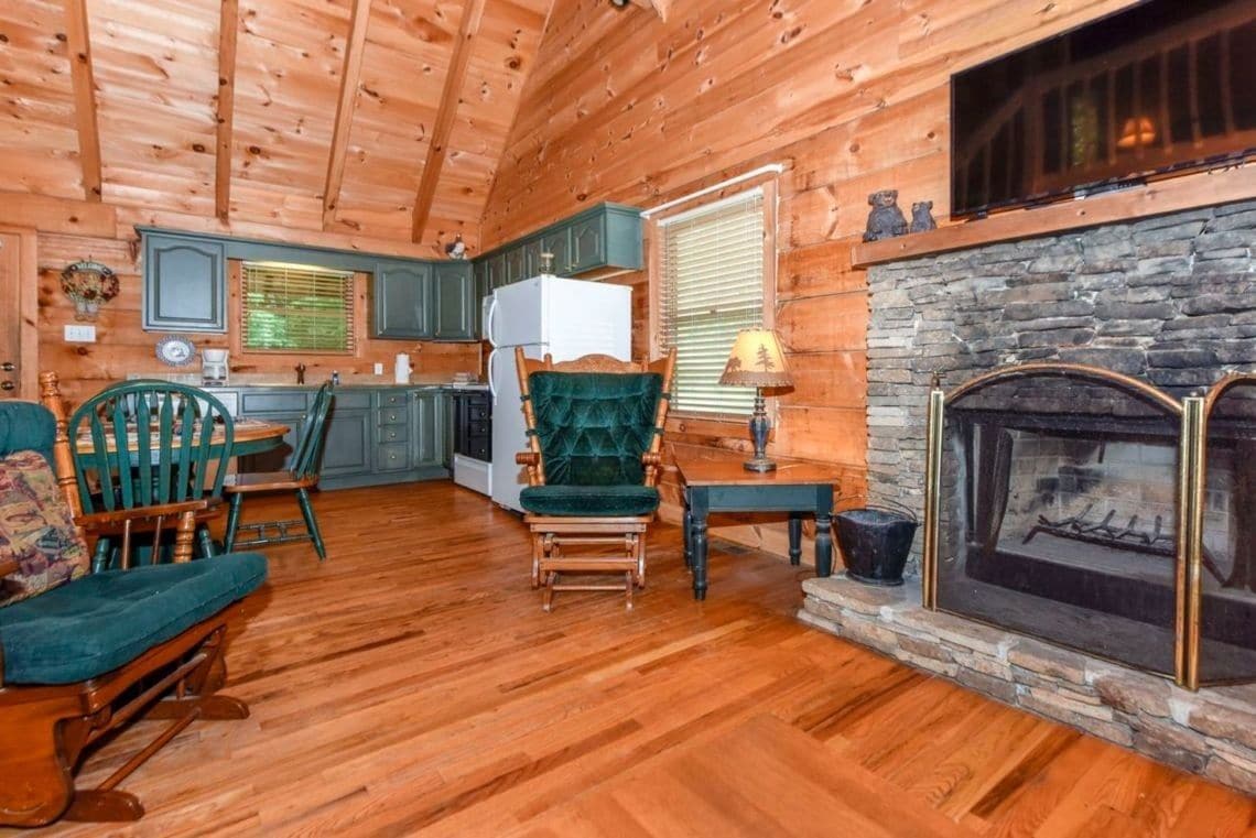 A log cabin interior with a dining area, kitchen, and fireplace.