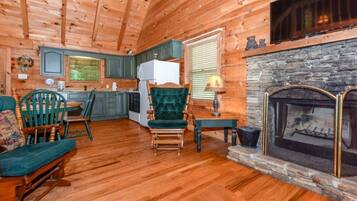 A log cabin interior with a dining area, kitchen, and fireplace.