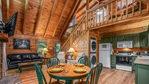A wooden cabin interior with a dining area, kitchen, and living room. - Willow Creek 2 Bedroom Cabin by RedAwning (Townsend)