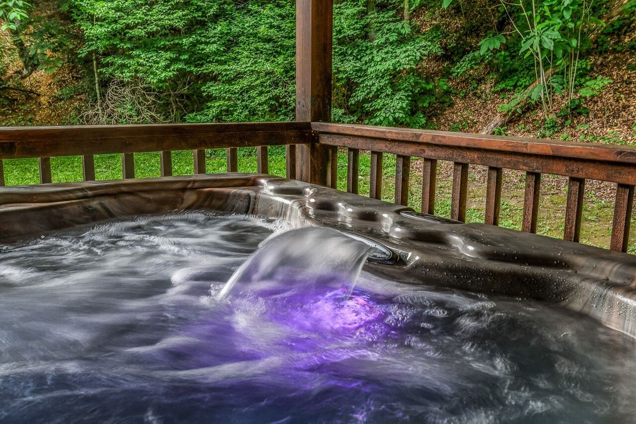 A hot tub with a wooden deck and a natural forest backdrop.