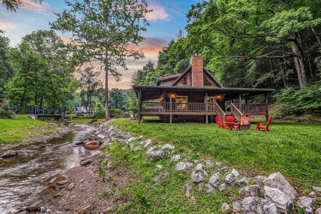 Eine Holzhütte mit Veranda, umgeben von Bäumen und einem Bach.
