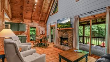 A cozy cabin interior with a stone fireplace, wooden floors, and a dining area.