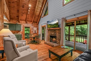 A cozy cabin interior with a stone fireplace, wooden floors, and a dining area.