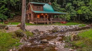 A rustic cabin with a porch, a small deck, and a view of a stream. - Willow Creek 2 Bedroom Cabin by RedAwning (Townsend)
