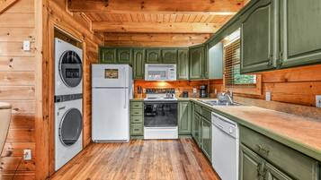 A compact kitchen with wooden walls, a washing machine, a microwave, a stove, and a dishwasher.