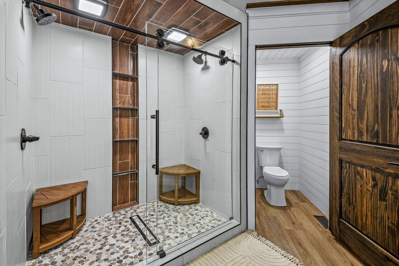 A bathroom with a shower, toilet, and a wooden cabinet.