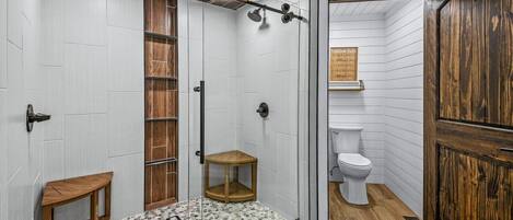 A bathroom with a shower, toilet, and a wooden cabinet.