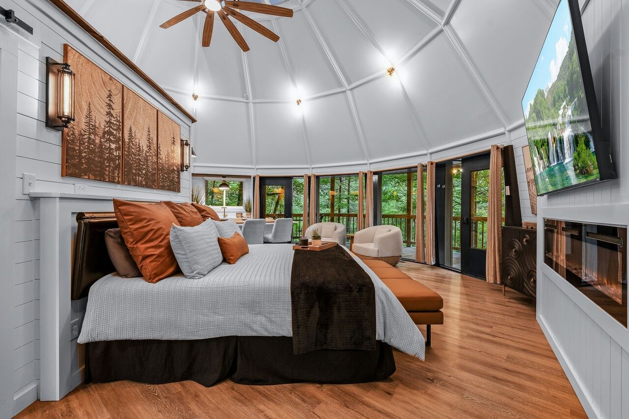 A spacious room with a large bed, a fireplace, and a television mounted on the wall.