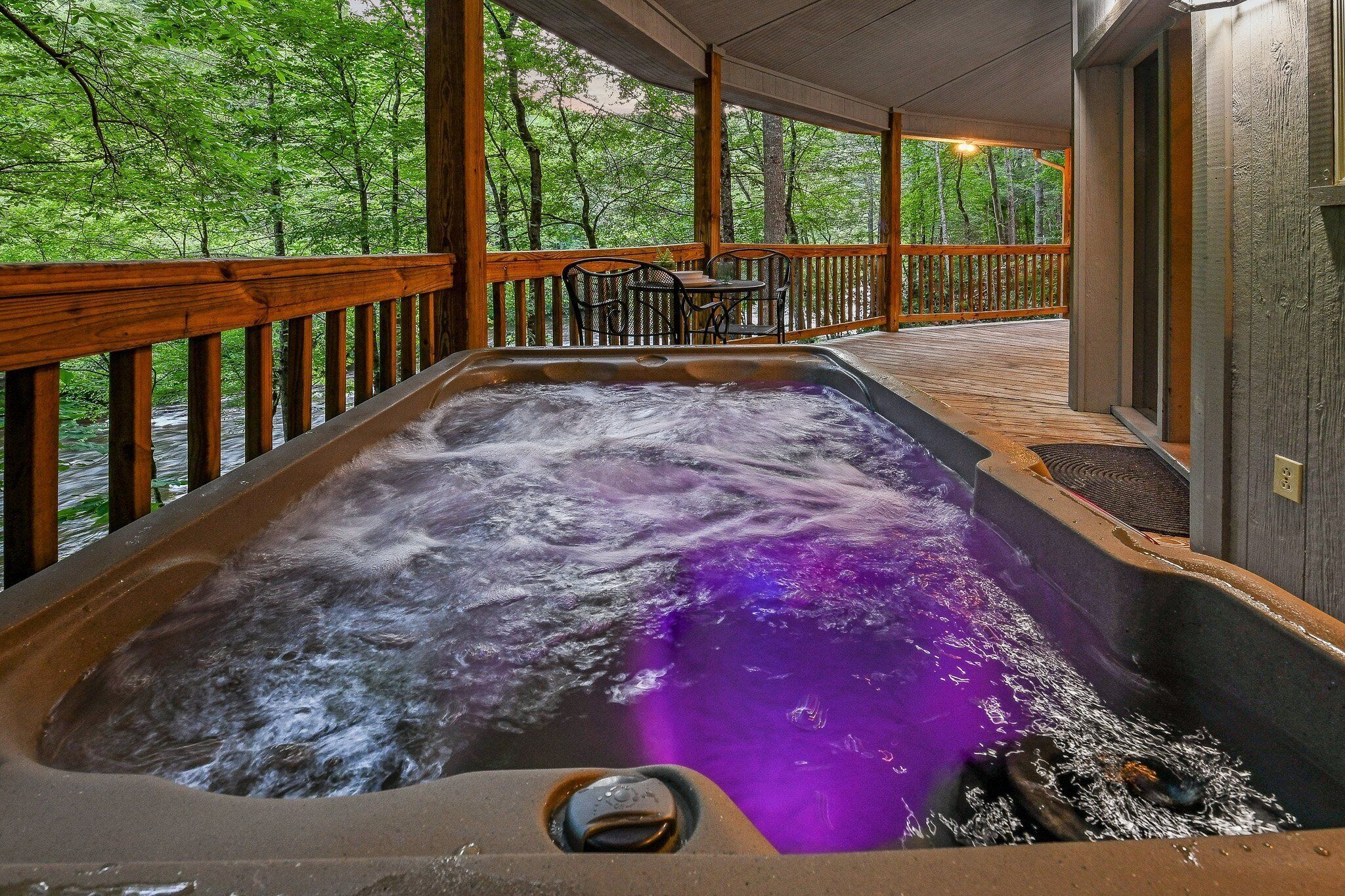 Ein Whirlpool mit Holzterrasse und Stühlen, umgeben von einem Wald.