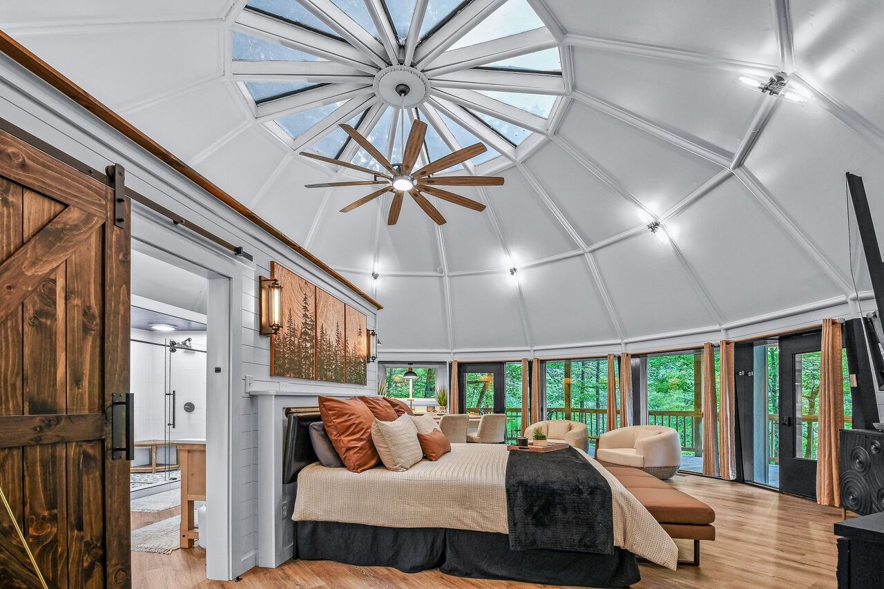 A spacious room with a large bed, a wooden ceiling fan, and a skylight.