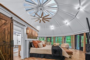 Un'ampia stanza con un grande letto, una ventola a soffitto in legno e un lucernario.