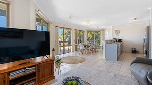 A spacious living area with a flat-screen TV, a dining table with chairs, and a kitchen area. - 69 Shepherd Ave Goolwa South (Goolwa South)
