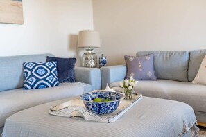 Relax in this serene living space with a light grey sofa, white side table, and a beautiful vase with white flowers.