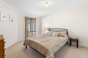 Une chambre à coucher comprenant un lit, une table de chevet, une lampe, une commode et une fenêtre avec des rideaux.