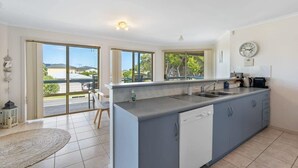 A modern kitchen with a large island, a dishwasher, and a sink. There are large windows providing a view of the outdoors. - 69 Shepherd Ave Goolwa South (Goolwa South)