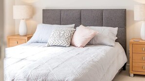 A bed with a grey upholstered headboard, a white quilted bedspread, and two bedside lamps on wooden nightstands. - 69 Shepherd Ave Goolwa South (Goolwa South)
