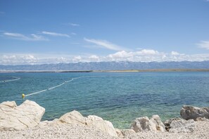 A coastal landscape with clear blue water, rocky foreground, and distant mountains. - Apartments Sana (Vir)