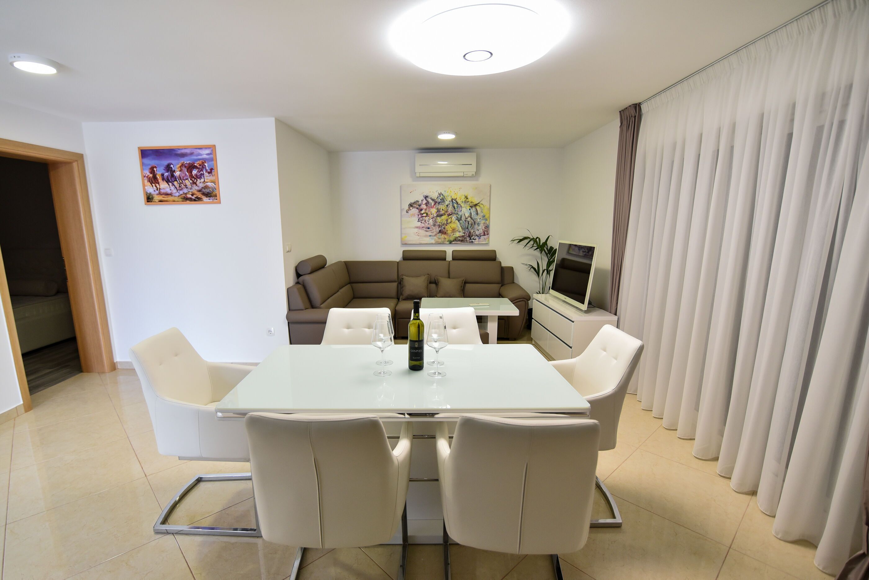 A modern dining area with a white table and chairs, a sofa, and a TV.
